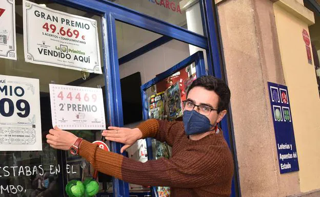 Javier Díaz coloca el cartel con el número ganador en la tienda mixta de la calle Talavera.  / DAVID PALMA