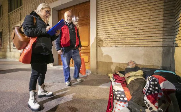 Un coordinador de Cruz Roja y un voluntario entrevistan a una persona que pernocta bajo los soportales de la Plaza del Pilar de Zaragoza